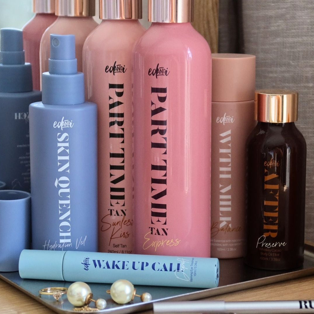 A collection of cosmetic and skincare bottles from the brand cofii, including 'PARTY TIME TAN', 'SKIN QUENCH', 'WAKE UP CALL', and 'RESJOUR' on a silver tray, set against a background of beige curtains.